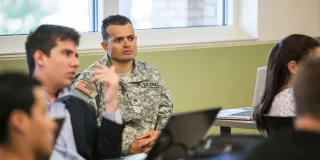 A photo of a U.S. Army soldier in uniform taking a course in a college classroom for the blog article on 'How does the Post-9/11 GI Bill work?' highlighting the eligibility requirements of this financial aid benefit for military-connected college students
